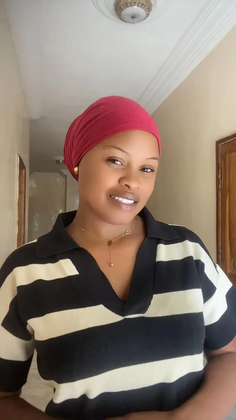 Rita smiling, wearing a red head wrap and a black-and-cream striped top