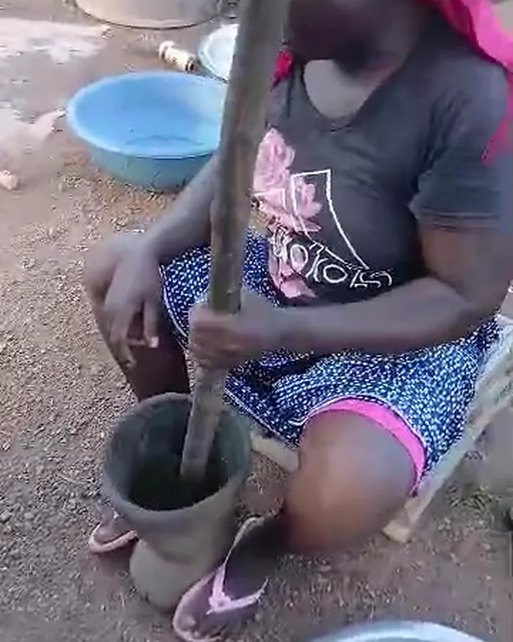 A woman pounding in a wooden mortar with a long pestle